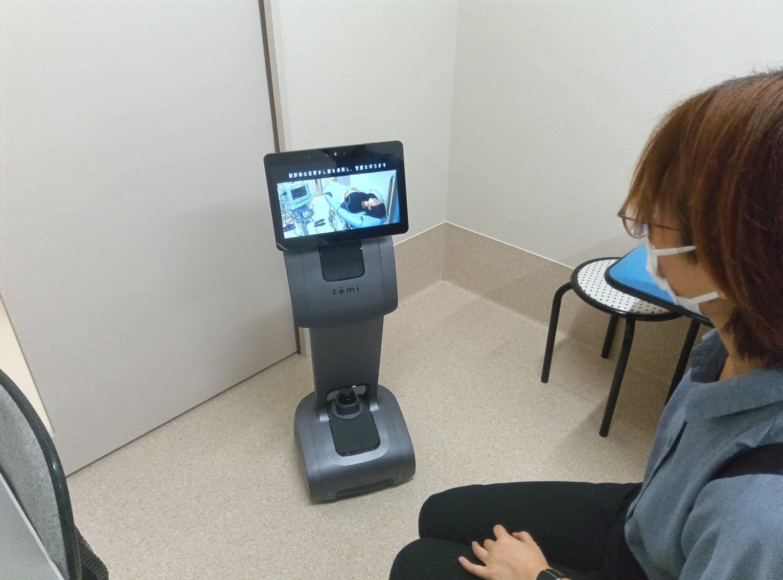 椅子に座った来院者が、目の前に立つ temi の画面を見ている