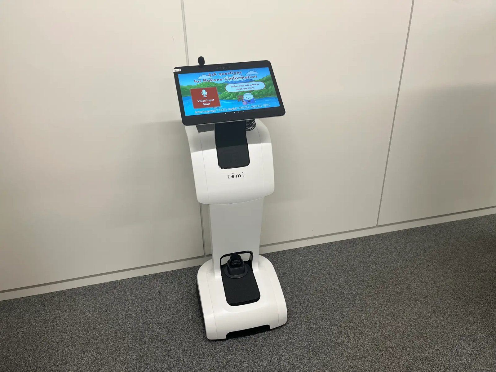 灰色のカーペットの上に立つ白い temi。画面には「Ask questions for Hakone's Information」の見出しと赤い音声入力ボタンが表示され、下に日本語・English などの言語選択が並んでいる